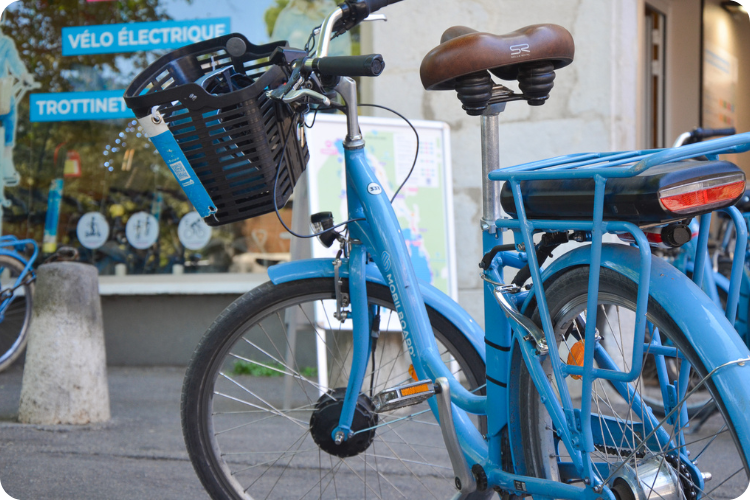Vélo de location bleu Mobilboard, panier avant et porte-bagages, devant la boutique à Annecy
